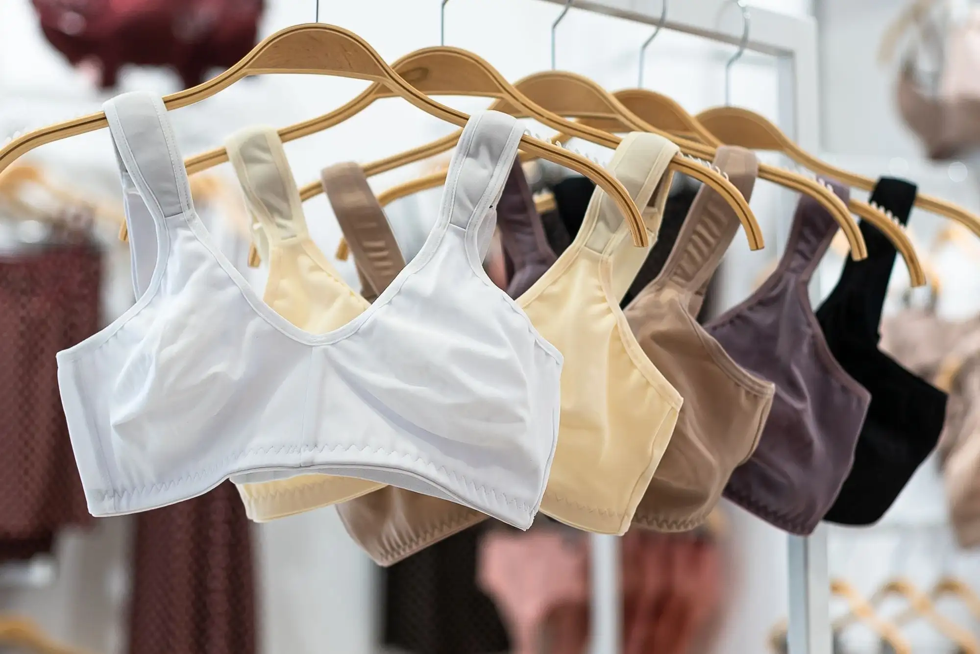Bløde bh'er i hvid, beige, brun, lilla og sort hænger på træbøjler i en butik