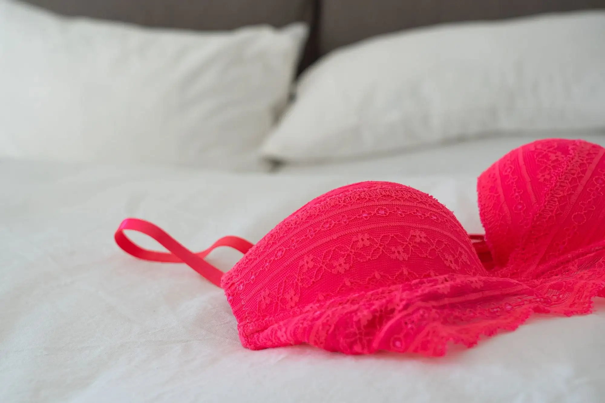 Pink blonde-bh med formstøbte skåle ligger på en hvid seng med puder i baggrunden